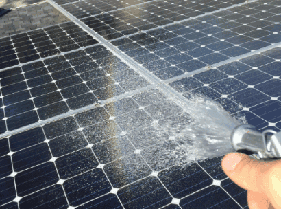 Person spraying water onto solar panels with a hose to clean them.