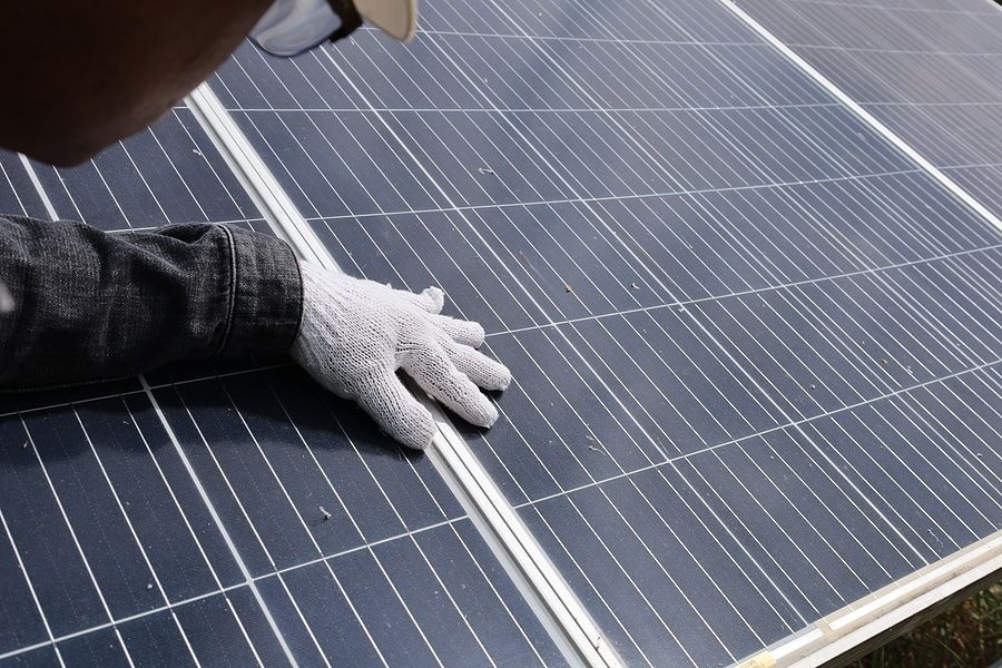 Close-up of a person wearing gloves inspecting a solar panel outdoors.